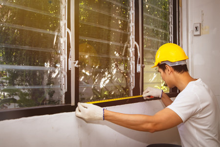 Carpenters put safety equipment in the workplace : Side view skilled carpenters, home dcor workers, use tape measure to measure the sill and louver to update it to a more modern windowの写真素材