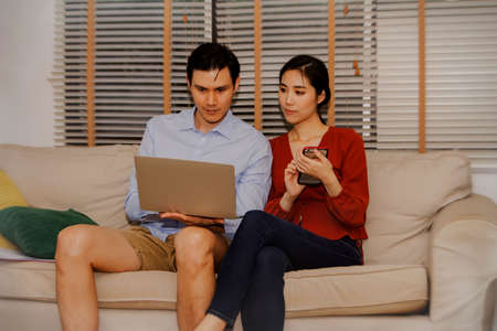Couples check out business analytics, online shopping, and trustworthy purchases from merchants looking for accurate information using laptop computers and smart phones at home : Selective Focusの写真素材