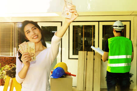 Renovation house concept : Beautiful asian women are happy with the cash availability of renovating and decorating an old white house, with an architect in charge of the design.の写真素材