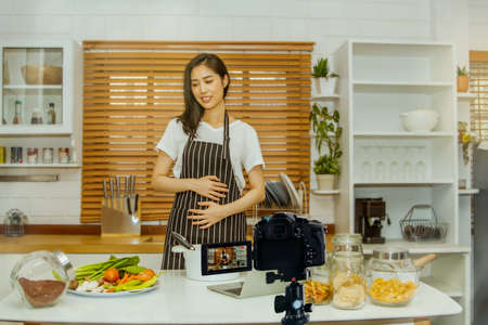 Concept of caring for the fetus : Beautiful Asian woman is pregnant, teaches useful cooking methods and video recordings from pregnant women for online media : Selective Focusの写真素材