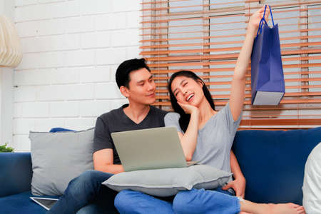 Couple uses their laptop to order additional luxury items after receiving them online and packed in a paper bag.の写真素材