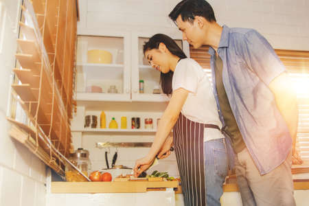 Family Love : Wife cooks breakfast in the kitchen happily, together with her husband standing behind : Wife cares about the food quality and nutrition of her beloved husband.の写真素材
