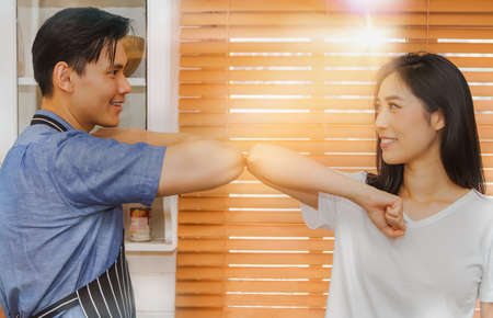 Couples have fun teasing together in the kitchen, hitting their elbows to avoid the spread of the coronavirus, greeting them with a hug or a handshake. Don't shake hands inside the houseの写真素材