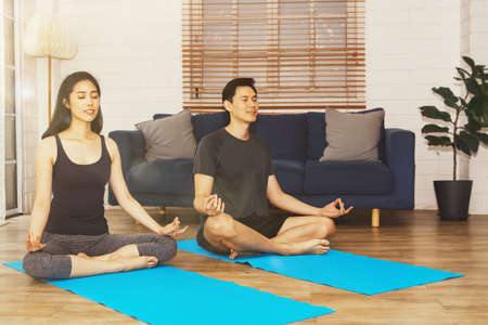 Yoga at home concept : Couple practicing meditation and yoga, calm their minds with lotus pose on a yoga mat in the living room.の写真素材