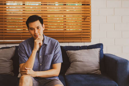 Portrait handsome Asian man sits and thinks about his own problem :  Personality man sitting on the sofa in his house uses his intelligence to solve problems with calmness.の写真素材