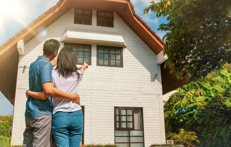 Living concept and family planning : Rear view Asian couple were proud to look at their beautiful two-story white house : Happy couple in new homeの写真素材