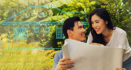 Happy Asian couple admires the blueprints of the beautifully designed houses. There is excitement, satisfaction and delight in getting a new home built on their land.の写真素材