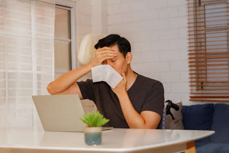 Sick men with high fever are likely to be infected with Coronavirus : Disabled man in a wheelchair is sick, has a fever, stuffy nose, sneezing, sneezing, holding toilet paper, wiping fluid on his noseの写真素材
