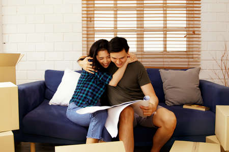Asian couple cuddled on a sofa and looked at the house plan, joyful that they had a new home.の写真素材