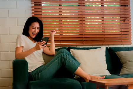 Young asian woman sits at home on a sofa with a smartphone, having fun she spends her free time relaxing and relaxing.の写真素材