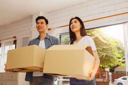 Happy moving day and starting a new life for the family concept : Happyness smiles of the couple as they walked in with a cardboard box and entered the door in their new white house in surprise.の写真素材