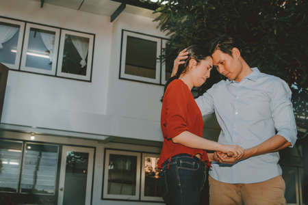 Couple husband and wife stand sad and sympathetic to each other while in front of the old house that has to be moved.の写真素材