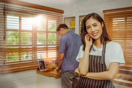 Concept happy couple in the kitchen :  Portrait of a young woman is satisfied that her husband cooks delicious meals for breakfast, making her stand proudly empty.の写真素材