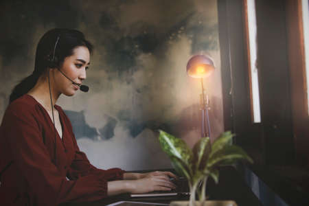 Side view Asian businesswoman wearing a wireless headset working at home with notebook computer job freelance, talks, video conference with clients : Selective Focusの写真素材