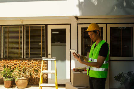 The male architect is in charge of the project, working on the renovation plan in front of the house, is writing down the repair list, renovating the house, and is preparing for work.の写真素材