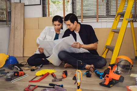 Asian couple looked at the house plan and had an idea to renovate the house to be beautiful : The two of them prepared all the necessary hand tools and electrical equipment on the wooden floor.の写真素材