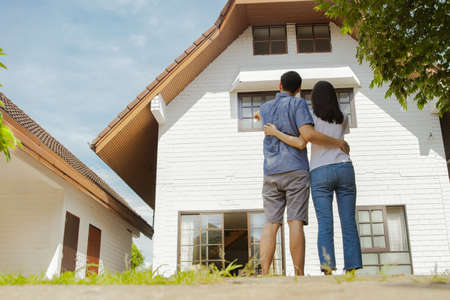 Rear view happiness, family, couples at home standing and hugging together looking at the new house modern white with happiness, ready to move inの写真素材