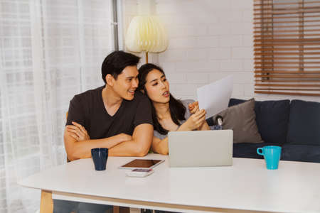Asian couples work online together to discuss online trade papers and do household chores with their laptops.Look for the details, look at the whitepaper: Couples plan their business and work from homの写真素材