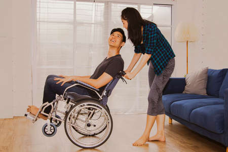 Love concept of a physically disabled couple : Relationship between a handicapped man and a beautiful woman playing tease together,Lift up the wheel of Wilchair with fun in his happy home.の写真素材
