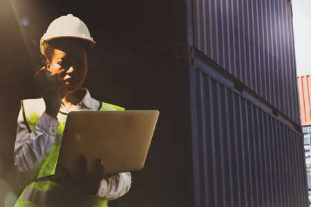 Portrait African American female workers, black foreman, reflective vest and helmet, use laptop and radio to control logistics,import,export,ship containers,order work and plan in the area.responsibleの写真素材