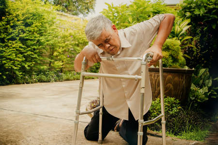 Elder Asian man who is in poor health with muccular dystrophy, rheumatoid arthritis and osteoporosis, slips on the white using a, walking aid trying to help himself : Health insurance conceptの写真素材