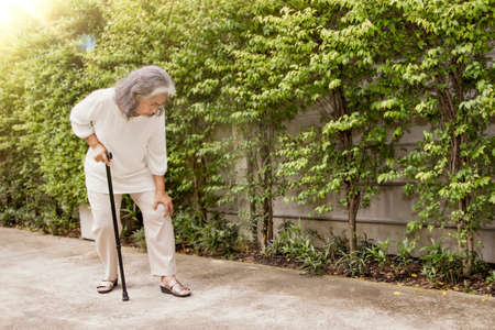 Senior Asian woman massaging her left knee with osteoarthritis during walking: knee injury, inflammation, more common in older people 60 years old : Health care concept: Selective Focus.の写真素材