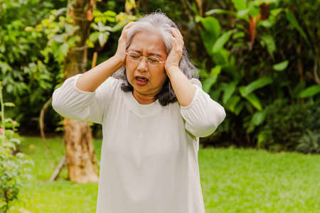 Elderly Asian woman in her 60's had a severe headache exacerbated her hand in pain, was suffering from a headache, and she had great patience : Concept of health problems, health care for the elderlyの写真素材