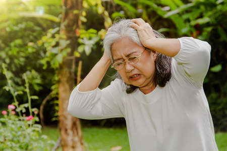 Elderly Asian woman in her 60's had a severe headache exacerbated her hand in pain, was suffering from a headache, and she had great patience : Concept of health problems, health care for the elderlyの写真素材