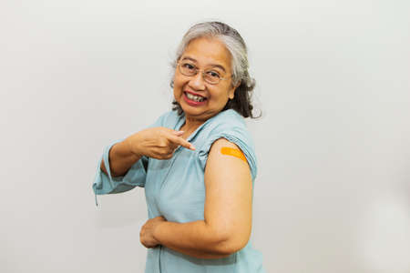 Asian elderly woman 60-70 years have been vaccinated against virus Points to the medicated plaster on the arm with the joy and joy of being immune to communicable disease.の写真素材
