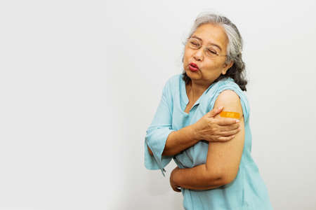 Elderly Asian woman aged 60-70 shows a sore face on her left arm that is covered with a medical plaster after receiving a vaccination from a doctor. Build immunity against virusの写真素材