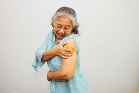 Elderly Asian woman aged 60-70 looks at her left arm covered with a medical plaster after receiving a vaccination from a doctor to immunize against the virus.の写真素材