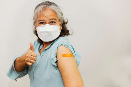 Portrait elderly asian woman wearing a mask has been vaccinated with the mRNA vaccine. virus on arm and covered with germ-resistant plaster, good health with thumbs upの写真素材