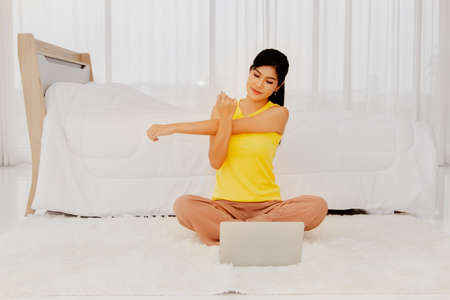 Long-haired beautiful woman stretched her arms to relax in the bedroom, using a laptop, computer, Internet online, follow these simple light exercise instructions.の写真素材
