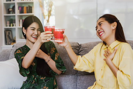 Joyful joy two beautiful Asian women smiling in their home ate ice-cold red nectar : Woman drinking sweet water quenches thirst : Selective Focusの写真素材