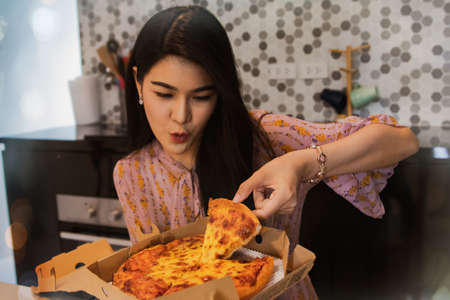Hungry asian woman eating pizza in kitchen : Long-haired woman is fasting but loves pizza with cheese.の写真素材