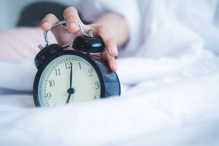 The hand of an Asian woman lying on a soft bed that keeps her in bed even when the clock wakes her.の写真素材