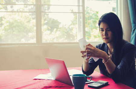 Young asian woman is worried about her spending too much at home : Her facial expression was stressful with financial problems and monthly debt and she crumpled the paper with sadness.の写真素材