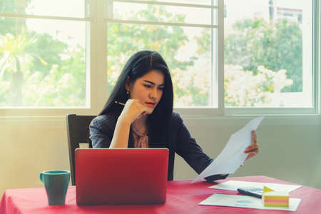 Portrait of Asian businesswoman looking at paperwork, graphing, finances, managing budgets, accountants working from home sitting at dining table : Work from home conceptの写真素材