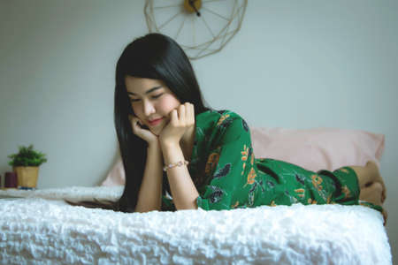 Beautiful woman wearing a comfortable green dress, sleeping, relaxing on a white bed inside the house and a quiet roomの写真素材