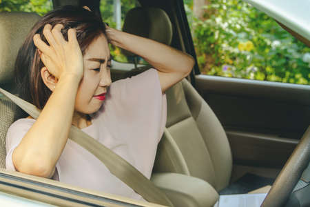 Asian woman is stressed out in a car with a debilitating problem that puts pressure on her.の写真素材