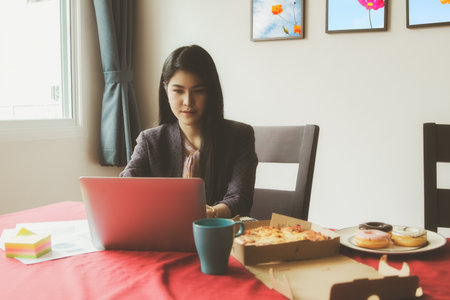 Businesswoman works at home, her office is sitting, working and planning easily on the table, with food and drinks ready to eat at all times.の写真素材