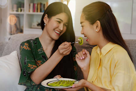 Smile portrait two beautiful Asian women ate in-house chopped fresh kiwi fruit as a snack, eating healthy fruit and adding vitamin C : Vitamin C and calcium from kiwifruit are beneficial for the body.の写真素材