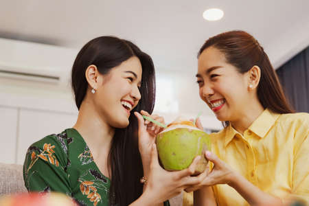 Women like to drink juice : Portrait two Asian women drinking fresh coconut water together in their home, laughing merrily.の写真素材