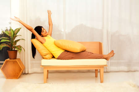 Happiness at home : Long-haired asian woman in a yellow shirt spends her time relaxing on the sofa at home, sitting or stretching out without work.の写真素材