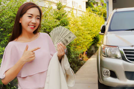 Asian business woman holds dollar bills and is well equipped in finance and management for auto insurance : Financial and loan insurance concept ; Selective Focusの写真素材
