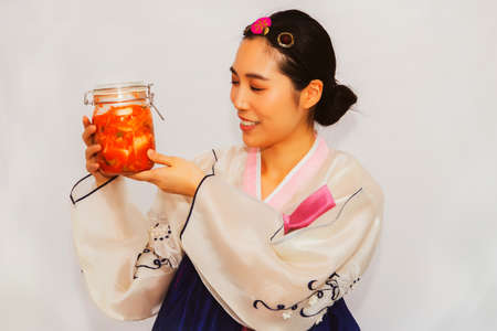 Happy portrait beautiful Asian woman wearing a Korean hanbok wants to taste the flavored kimchi in a glass bowl.の写真素材