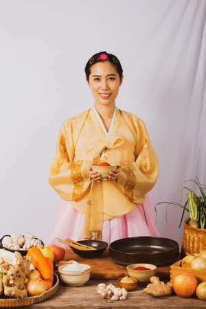 Portrait korean asian beautiful woman wearing golden hanbok, preparing food, folk wisdom Korean Recipes Kimchi Pickles, she is happy, ready to cook homemade carefully and deliberately.の写真素材