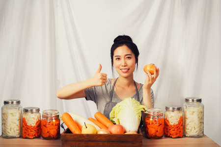 Asian women prepare quality fresh ingredients. Cook up a traditional Korean kimchi recipe, cut carrots and radishes and put them in a glass jarの写真素材