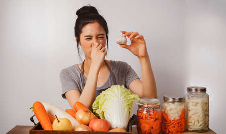 Image of the cuteness of young asian woman prepares the ingredients for kimchi with white garlic as a food ingredient. She feels the pungent smell of her nose.の写真素材