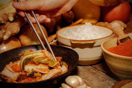 Close-up of a woman's hand using chopsticks to taste kimchi, a traditional recipe of Korean culture.の写真素材
